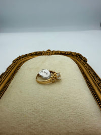 14k This is a yellow gold engagement ring with a round brilliant cut center (Cz) stone and decorative floral or plumeria-style side motifs.